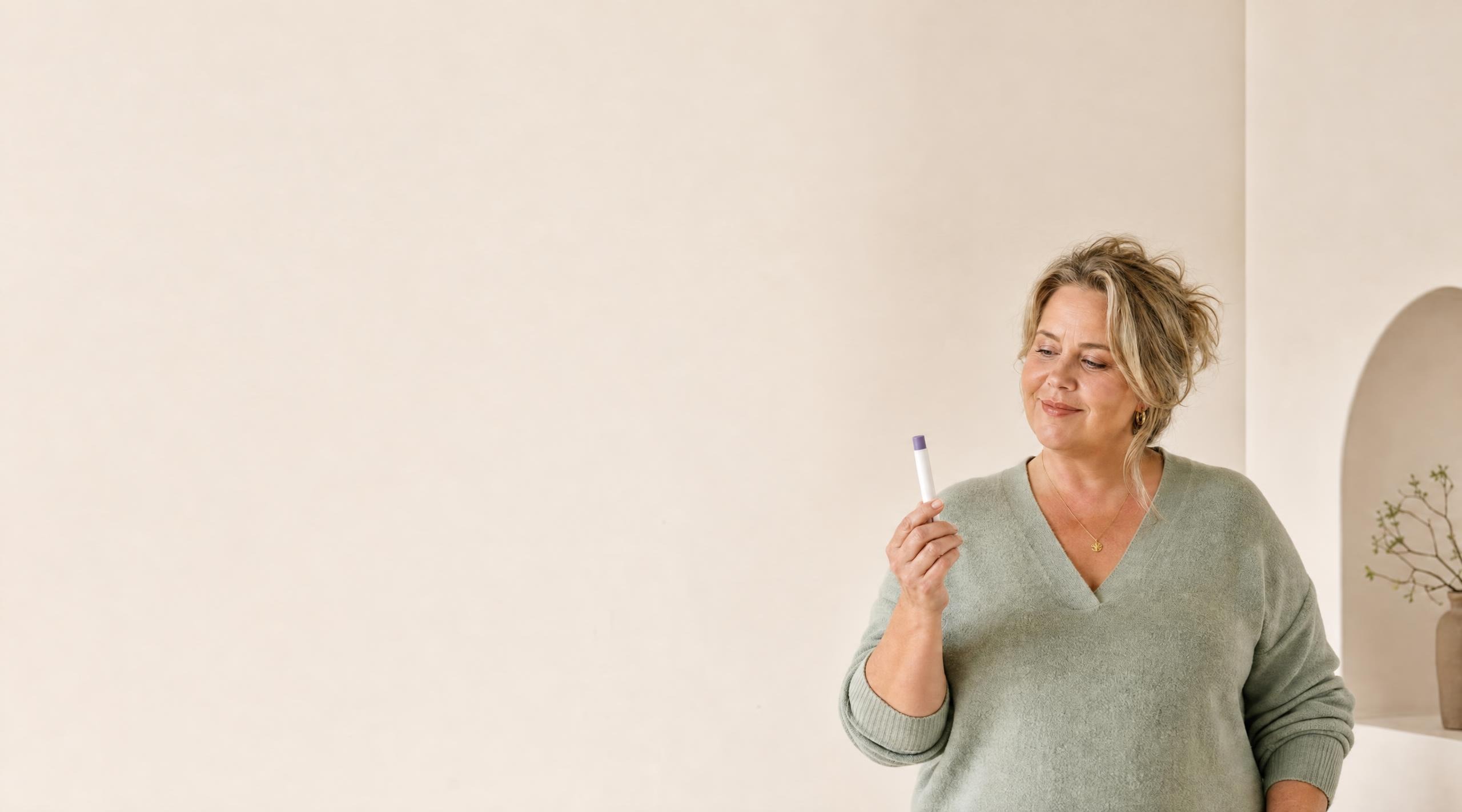 Vrouw houdt een injectiepen voor medisch afvallen vast tegen een rustige beige achtergrond