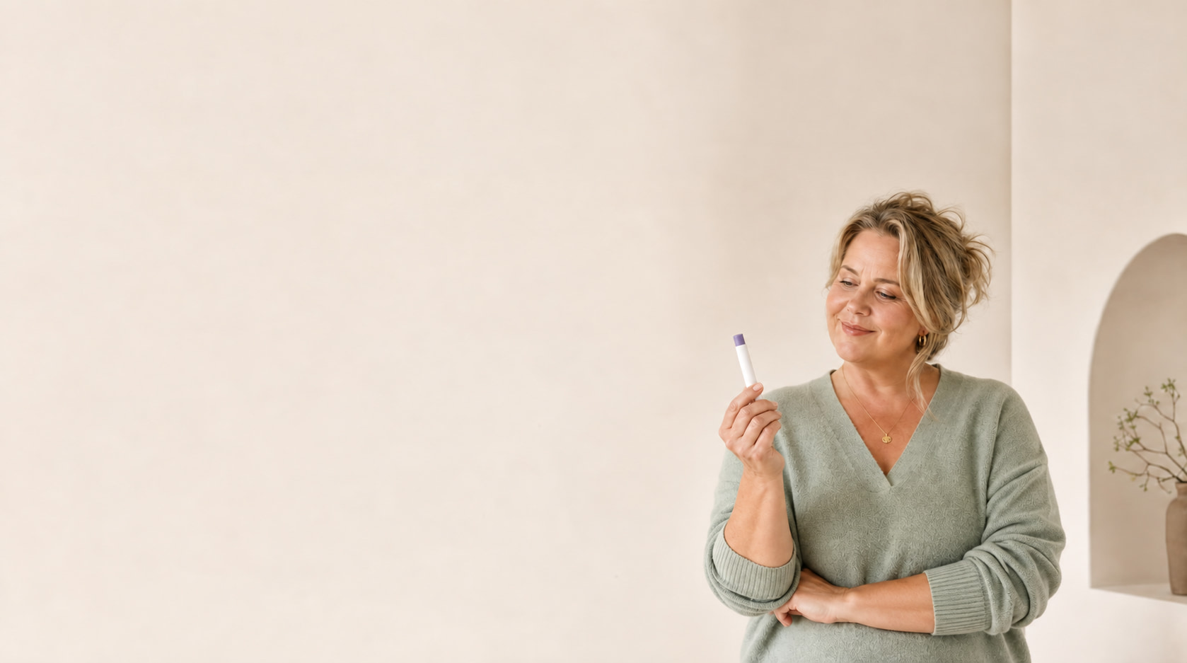 Woman in her fifties smiling as she looks at an injection pen for medical weight loss against a calm beige background